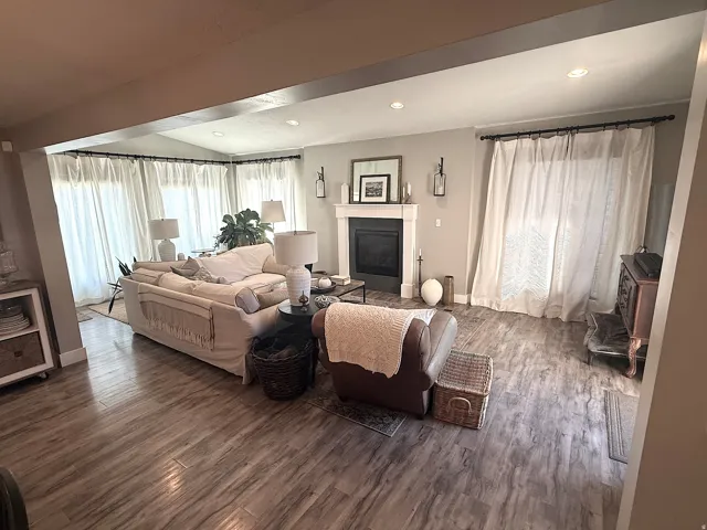 Spacious living area featuring wood-finish flooring, a fireplace with a white mantel, and recessed lighting