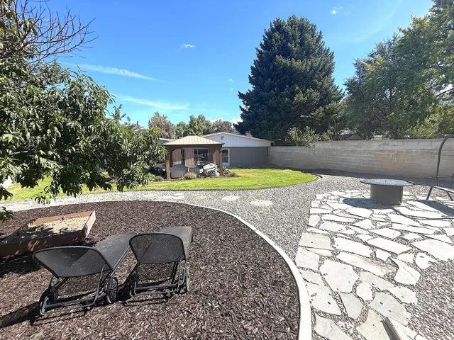 Backyard featuring a stone-paved patio, gravel path, and manicured lawn