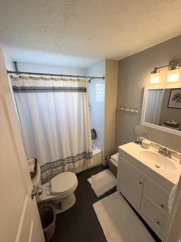 Vanity with integrated sink, modern wall-mounted light fixture, subway tile shower surround, glass block window, and dark tile flooring