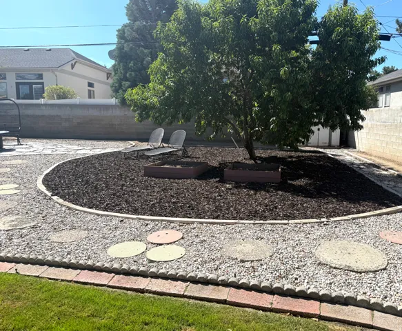 Landscaped backyard featuring a mature tree, wood chip ground cover, gravel pathways, and decorative stepping stones
