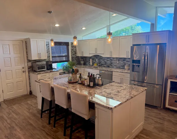 Kitchen featuring white cabinetry, a large kitchen island with a stone countertop, wood-finish flooring, stainless steel appliances, and a tile backsplash