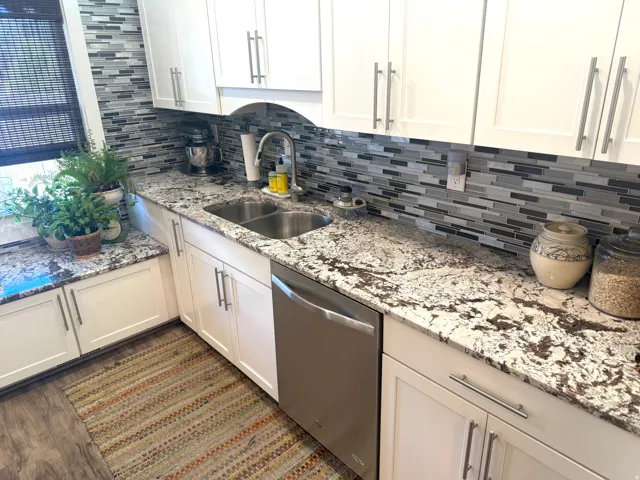 White shaker cabinetry, stainless steel double basin sink, mosaic tile backsplash, wood-finish flooring, and light-toned countertops
