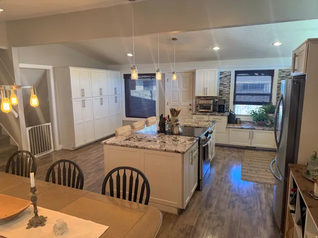 Kitchen featuring white cabinetry, granite countertops, stainless steel appliances, wood-finish flooring, and a stone-tile backsplash
