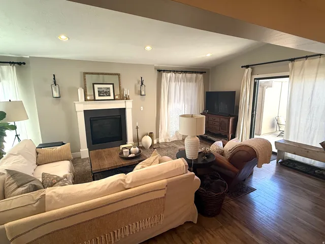 Recessed lighting illuminates the living space featuring a fireplace with a white mantel and black surround, wood-finish flooring, and multiple sliding glass doors