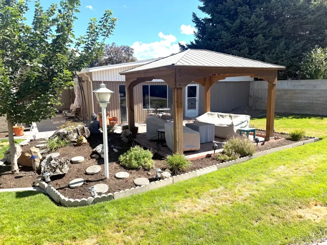 Expansive backyard featuring a wood-frame gazebo with a metal roof, brick paver patio, and decorative landscaping with stepping stones