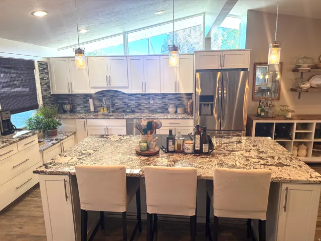 Spacious kitchen featuring a large island with seating, white shaker-style cabinetry, granite countertops, and stainless steel appliances