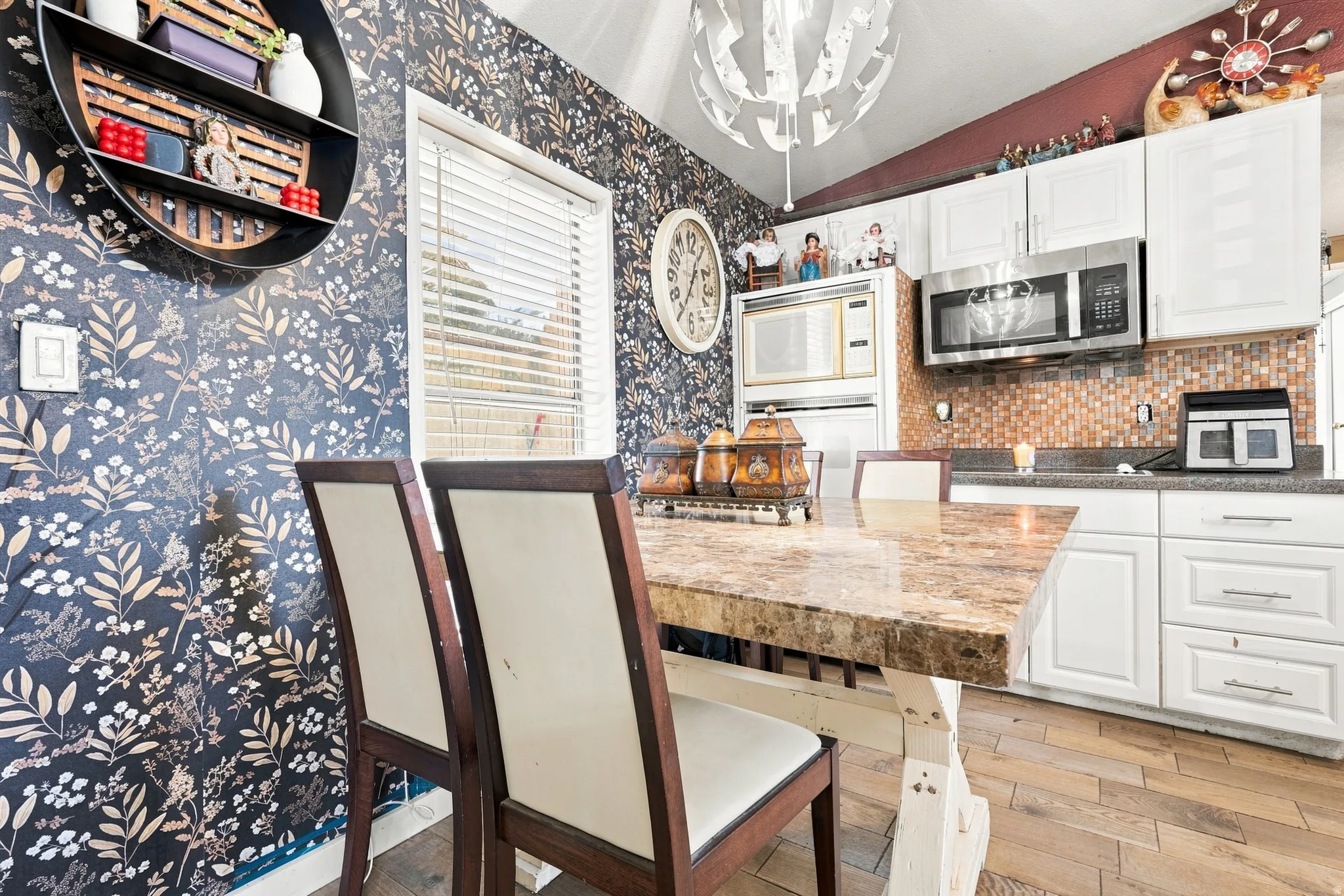 Kitchen featuring white cabinetry, stainless steel microwave, stone mosaic tile backsplash, wood-finish flooring, and a stone-top island