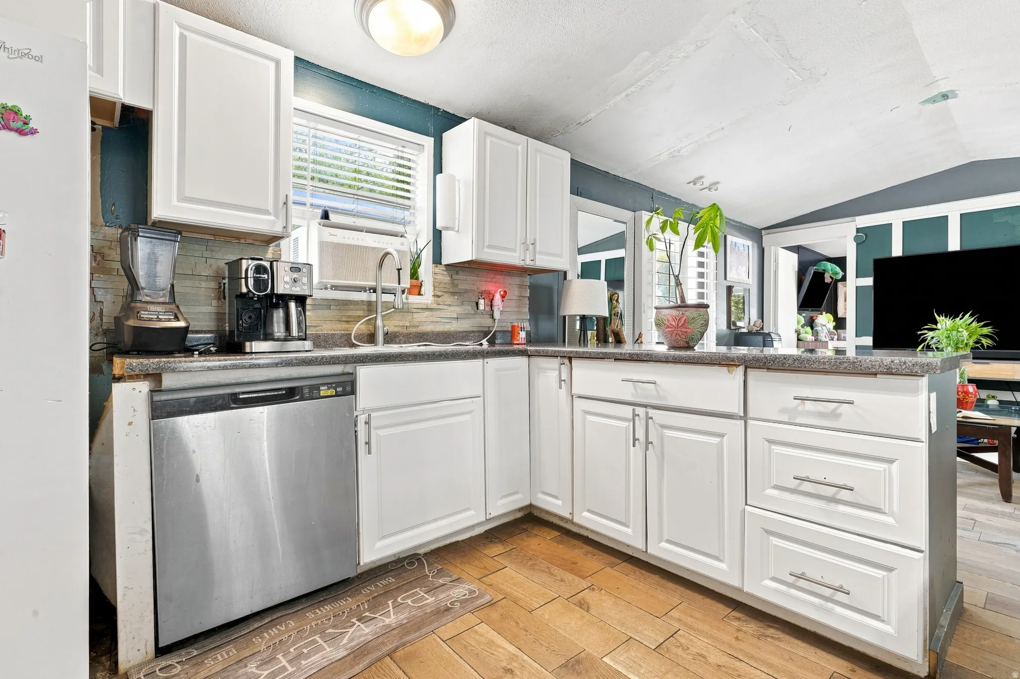 White cabinetry, stainless steel dishwasher, tile backsplash, wood-finish flooring, and recessed lighting