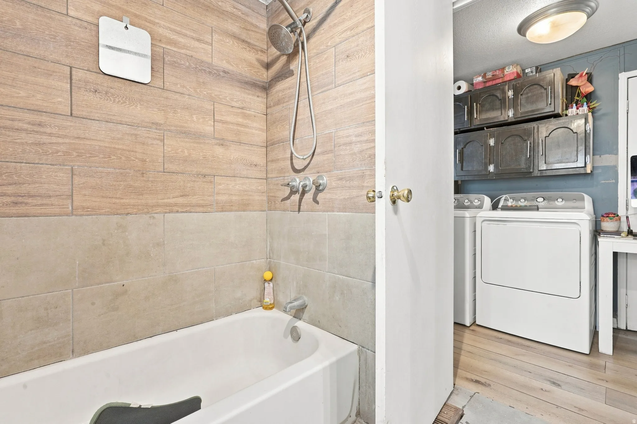 Bathtub with a shower fixture, wood-finish tile wall, and complementary tile surround