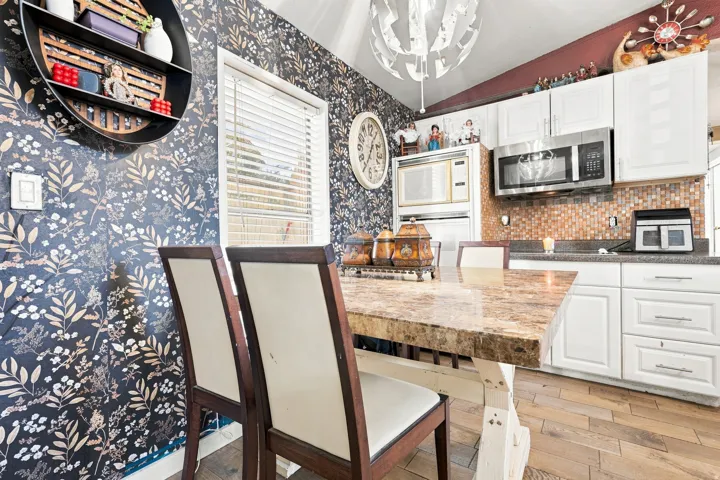 Kitchen featuring white cabinetry, stainless steel microwave, stone mosaic tile backsplash, wood-finish flooring, and a stone-top island