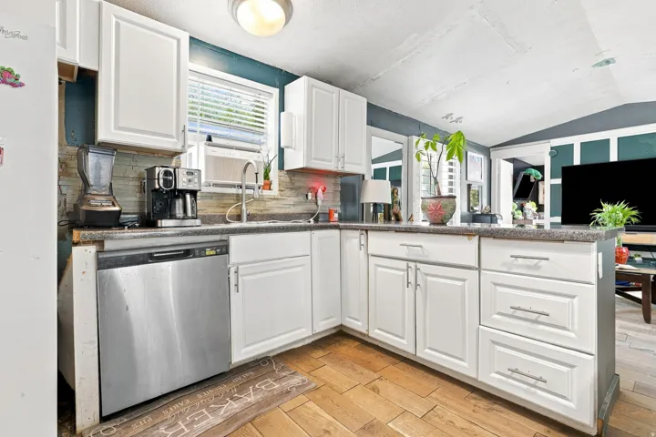 White cabinetry, stainless steel dishwasher, tile backsplash, wood-finish flooring, and recessed lighting
