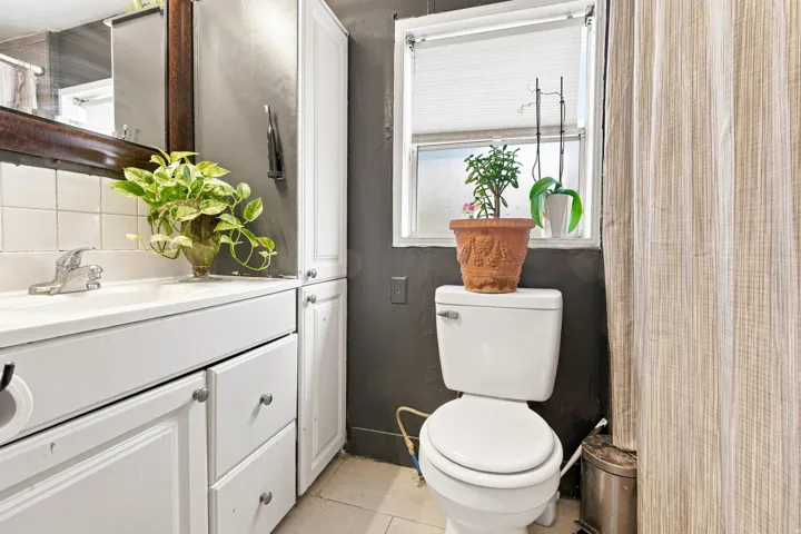 White vanity with integrated sink, white tile backsplash, built-in storage cabinetry, and a window for natural light
