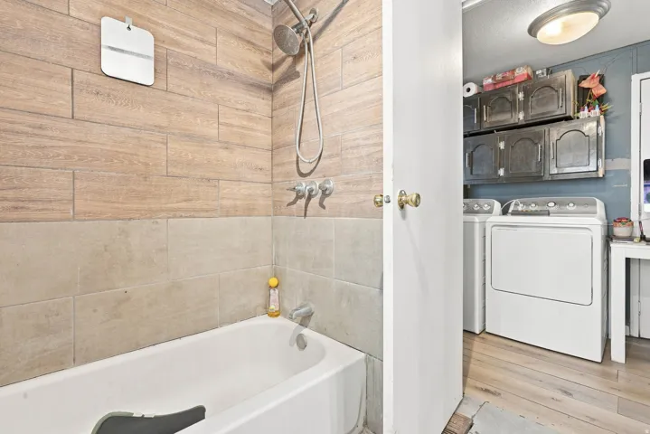 Bathtub with a shower fixture, wood-finish tile wall, and complementary tile surround