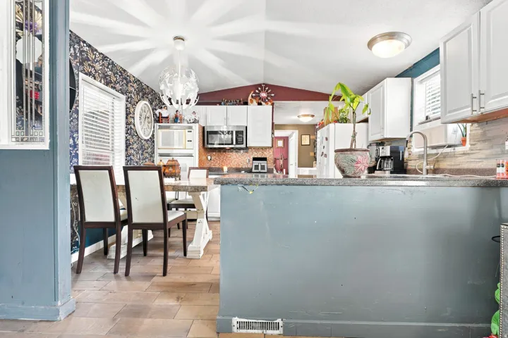 Wood-finish flooring throughout, white upper cabinetry, stainless steel appliances, and a kitchen island with a sink and faucet