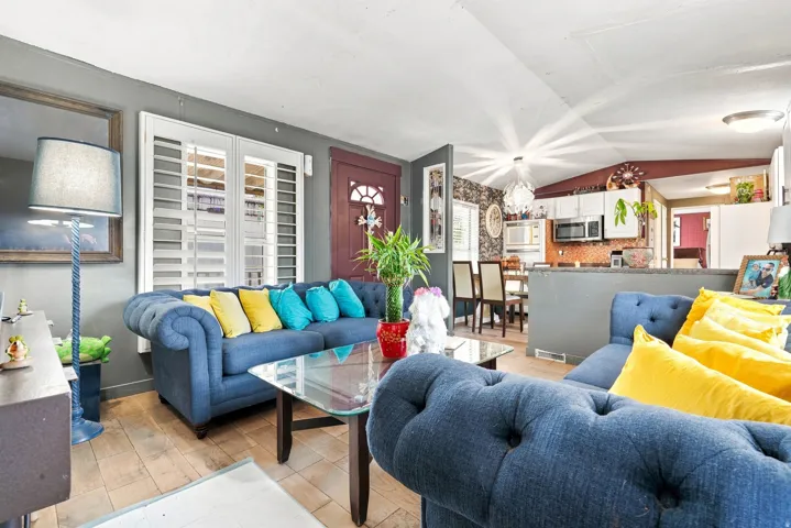 Open-concept living area with wood-finish flooring, white plantation shutters, and a built-in kitchen pass-through