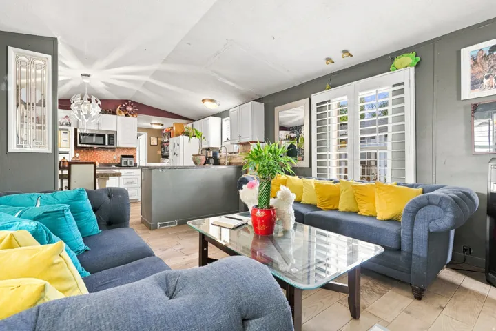 Living area with wood-finish flooring, vaulted ceiling, and white louvered window treatments