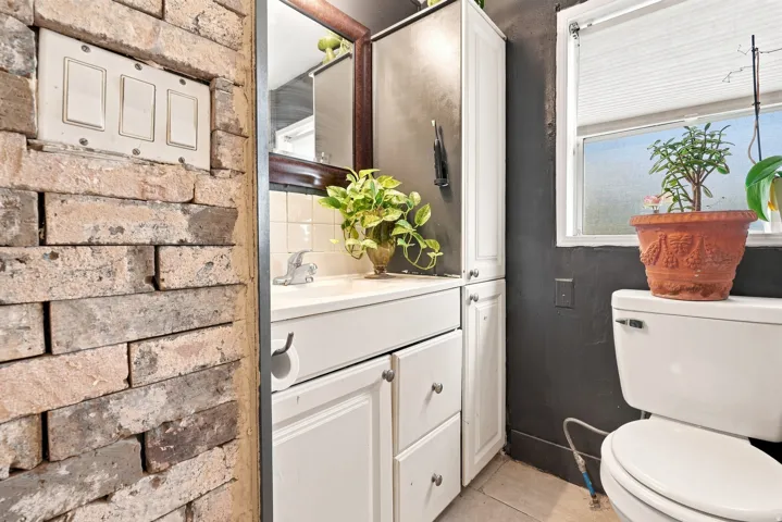 Exposed brick wall detail, white vanity with integrated sink, white storage cabinetry, and a window with privacy blinds