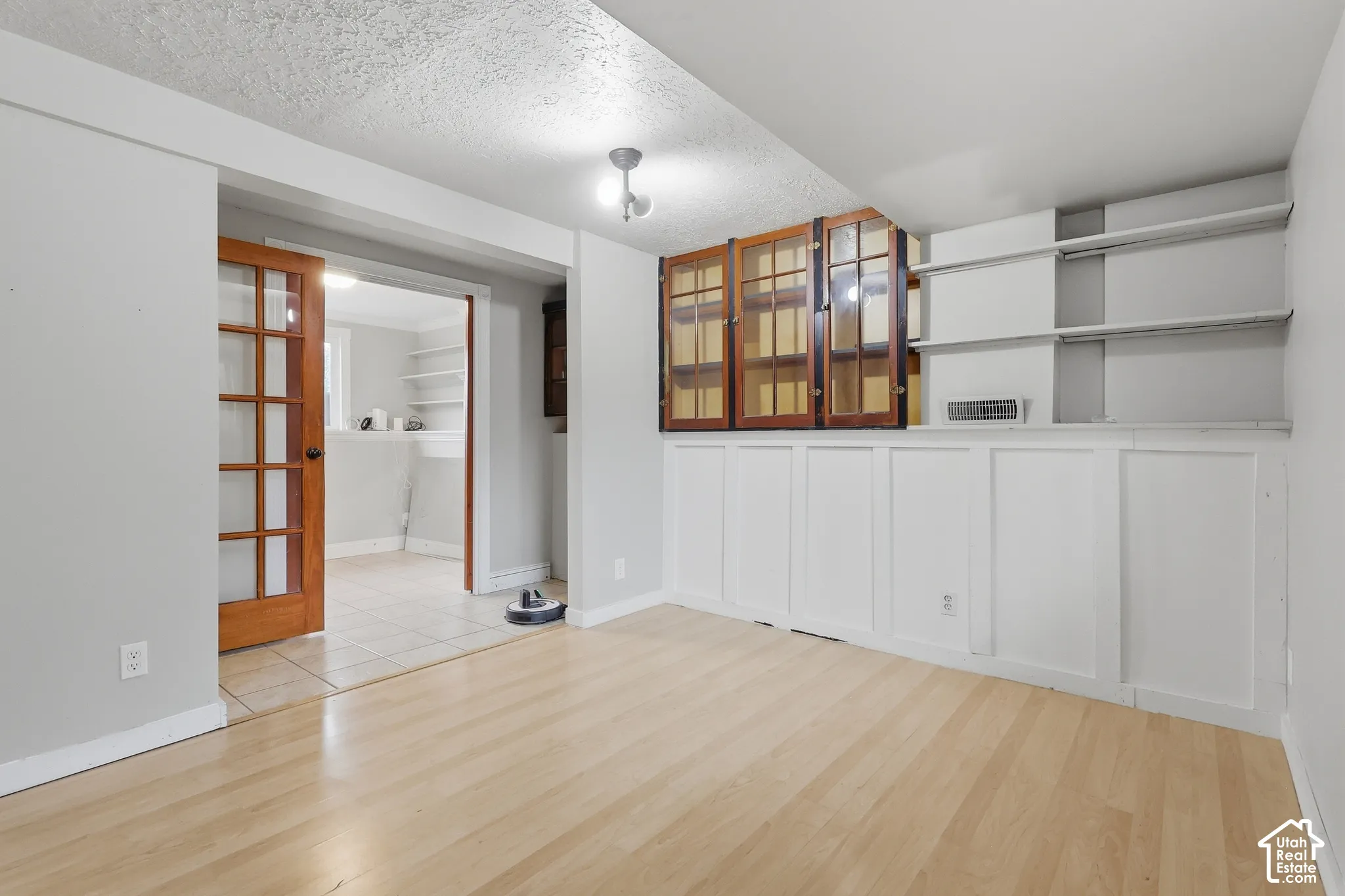 Wood-finish flooring, white paneling, built-in shelving, wood-frame glass-paneled door, and overhead lighting