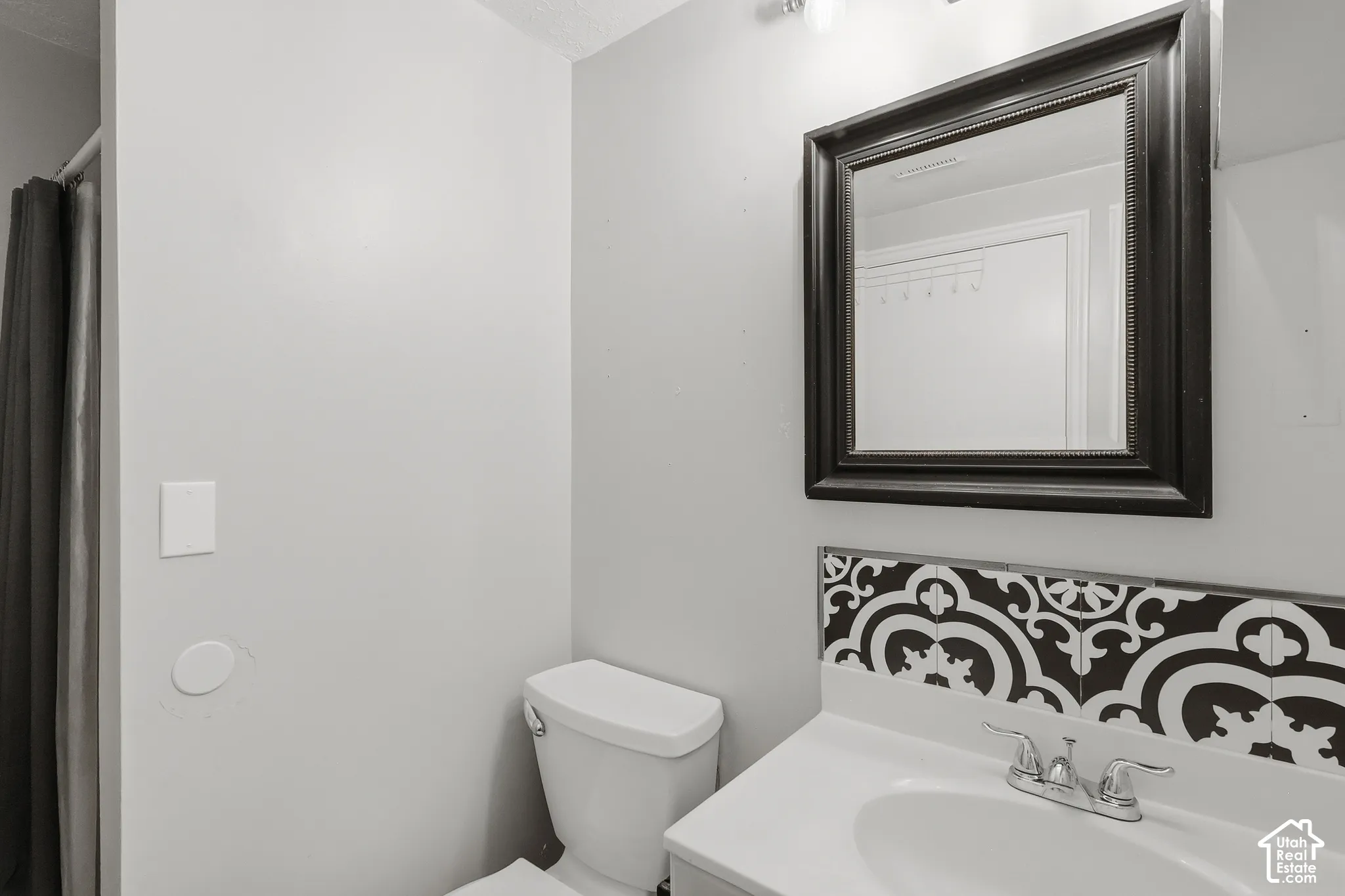 Bathroom featuring a vanity with a white countertop and integrated sink, chrome faucet, patterned tile backsplash, and a framed mirror