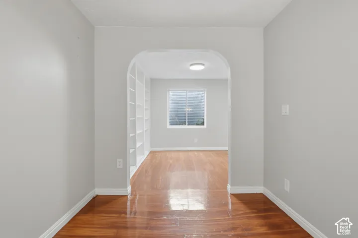 Archway entry to a room with wood-finish flooring, built-in shelving, and a single window