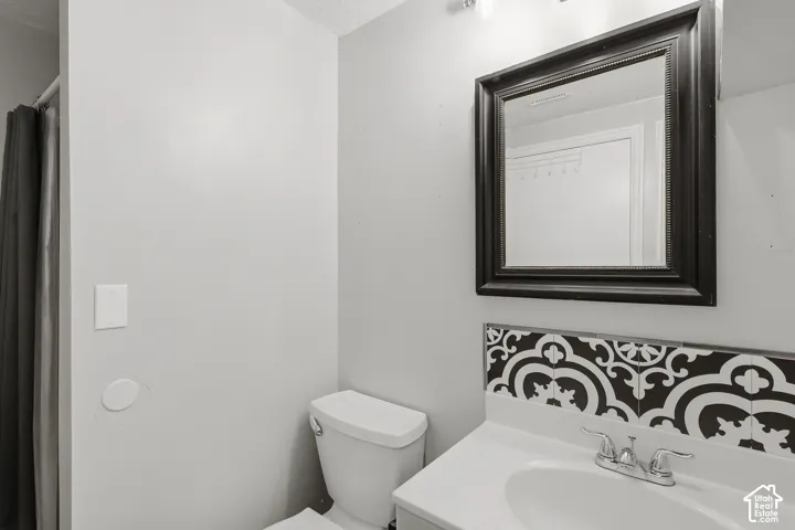 Bathroom featuring a vanity with a white countertop and integrated sink, chrome faucet, patterned tile backsplash, and a framed mirror