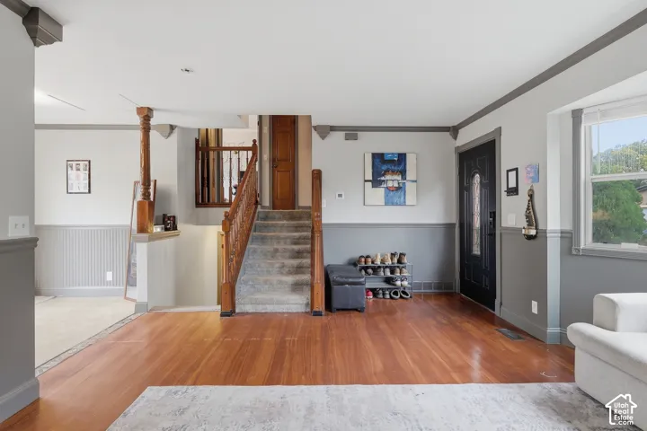 Hardwood flooring, wainscoting, a paneled front door with decorative glass, and a carpeted staircase with wood banister