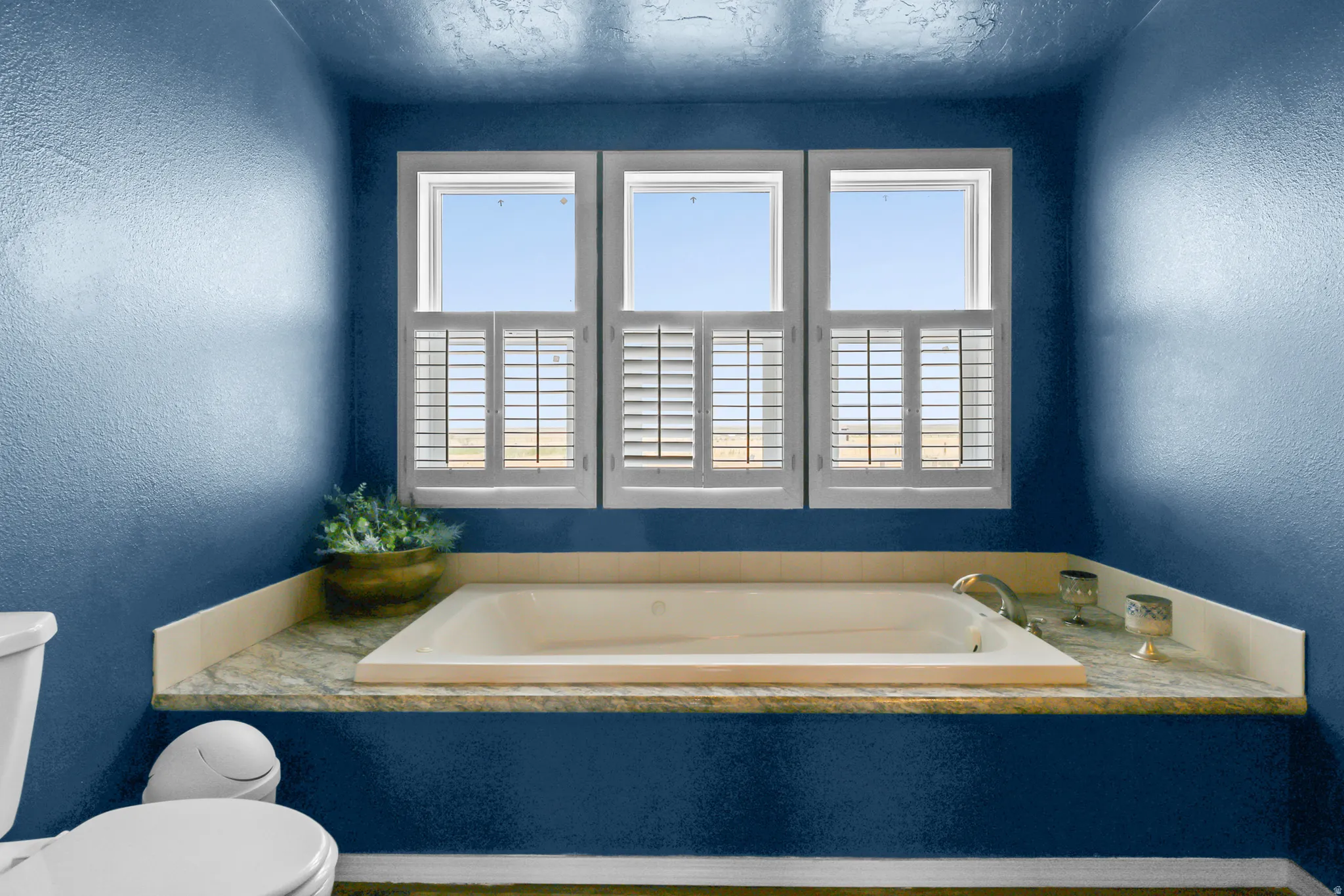 Built-in soaking tub with deck-mounted faucet, surrounded by a stone-finish countertop