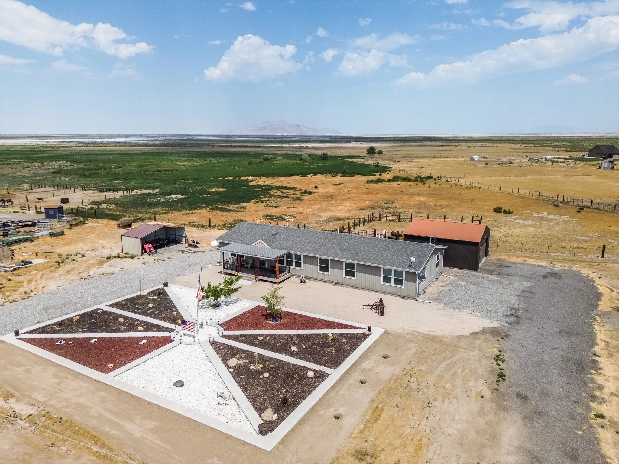Ranch-style residence featuring a covered front porch, gravel pathways, a decorative rock garden, two detached outbuildings, and a surrounding expansive terrain