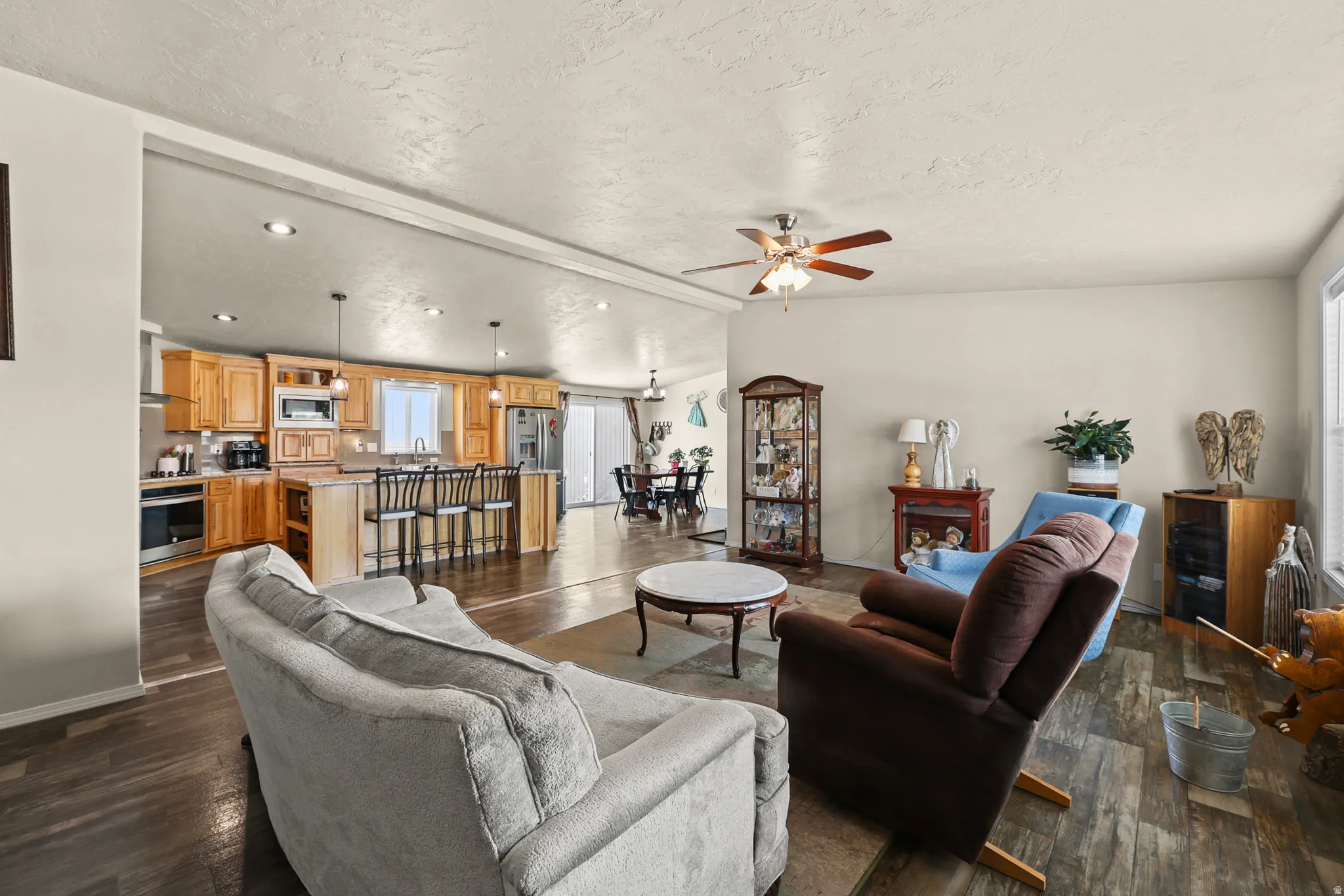 Open-concept design featuring wood-finish flooring, recessed lighting, a ceiling fan, and a kitchen with wood cabinetry and an island with seating