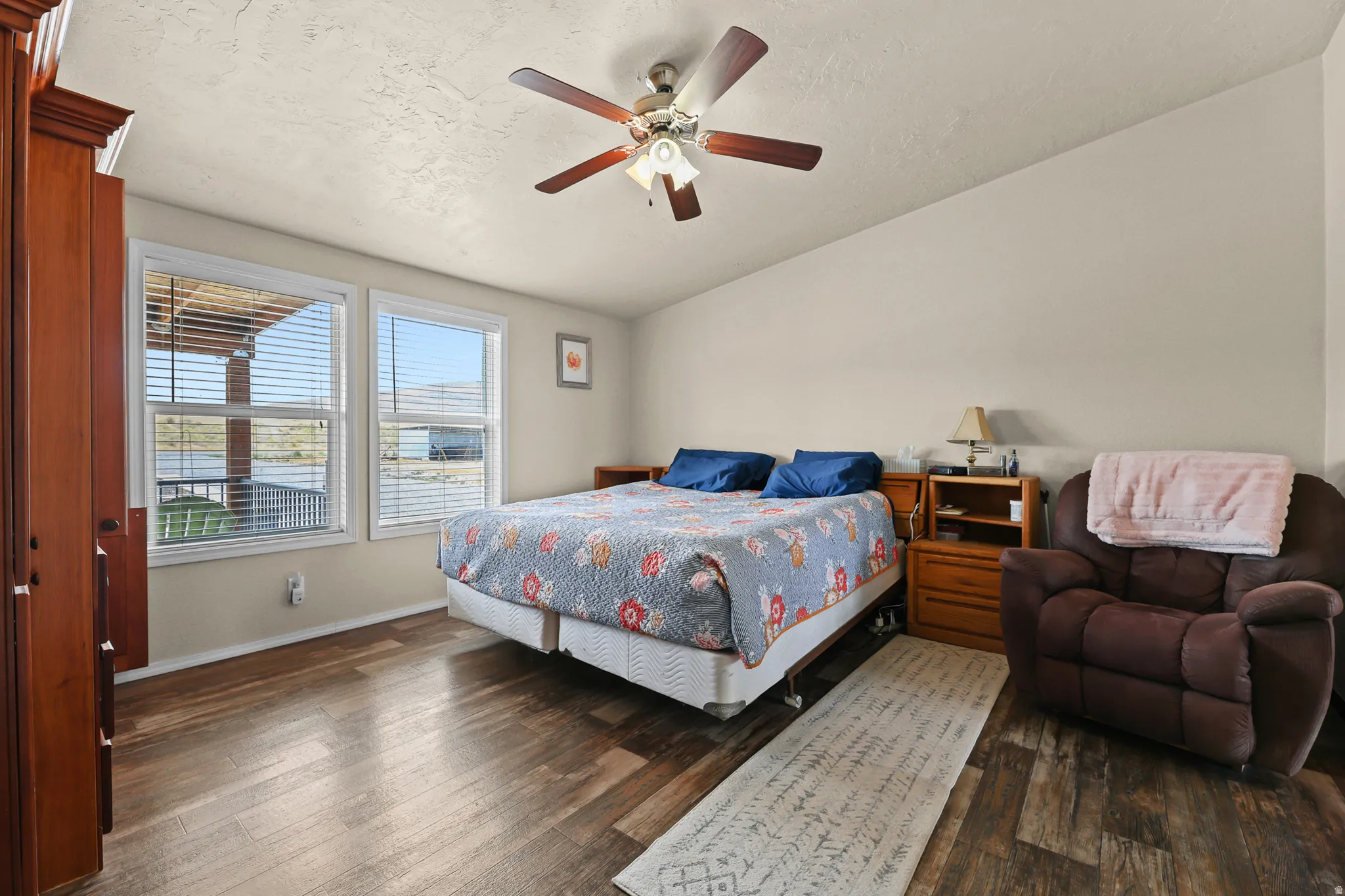 Wood-finish flooring, dual windows with horizontal blinds, sloped ceiling, and a ceiling fan