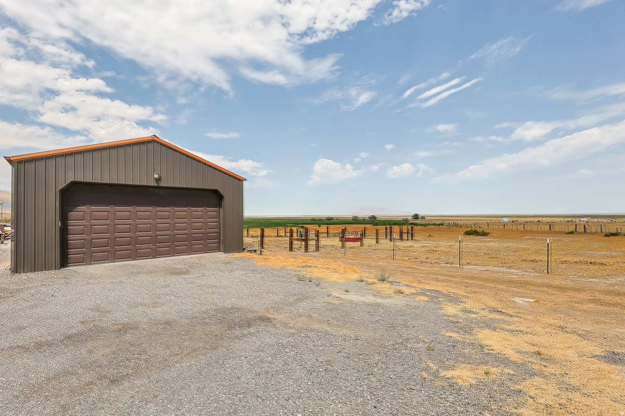 Metal-clad outbuilding with a brown garage door, gravel foreground, and expansive open terrain