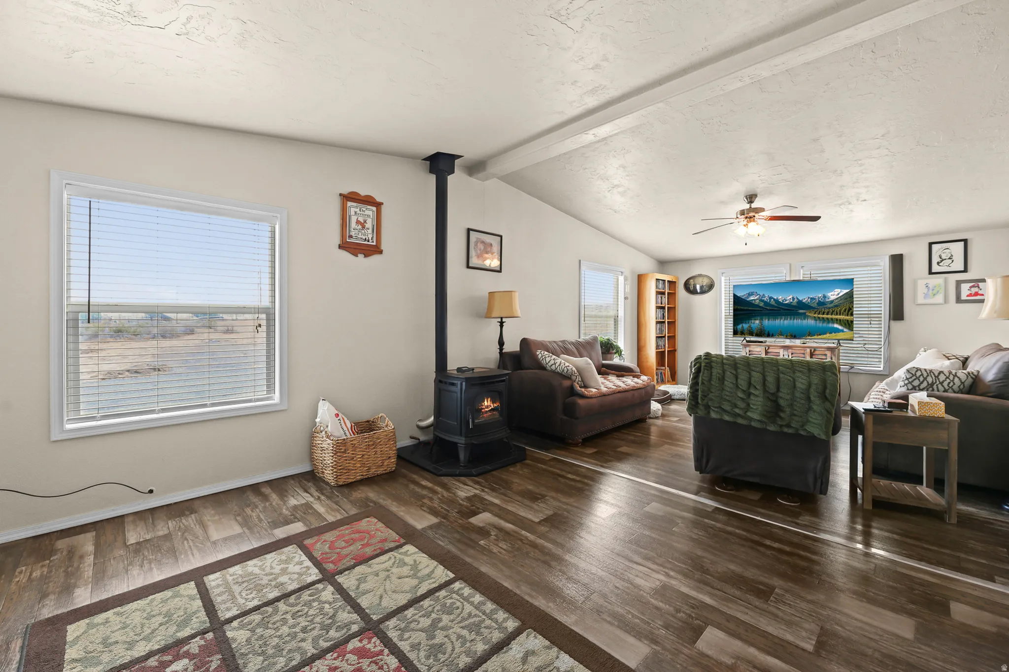 Spacious living area featuring wood-finish flooring, a wood-burning stove, and multiple windows