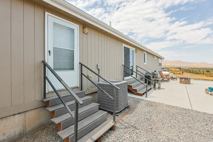 Exterior featuring light beige vertical siding, two outdoor staircases with black railings, and a concrete patio with a built-in stone fire pit