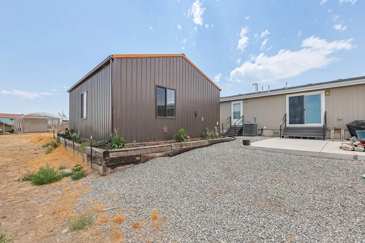 Brown corrugated metal siding structure, raised wood-tie planter beds, gravel ground cover, concrete patio, and sliding glass door access