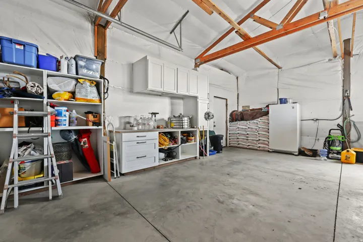 Exposed wood beam ceiling, white wall paneling, built-in white cabinetry, built-in open shelving, and a concrete floor