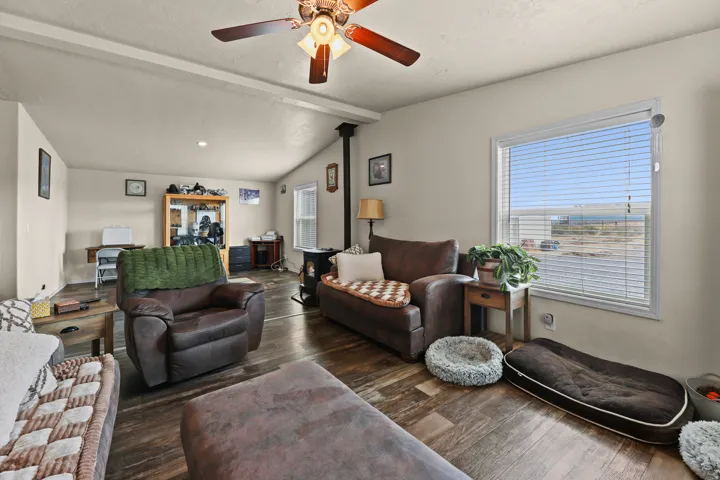 Vaulted ceiling with exposed beams, wood-finish flooring, and a ceiling fan with light fixture