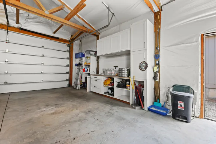 Garage featuring a concrete floor, exposed wood beam ceiling, white sectional garage door, and built-in white cabinetry with a countertop