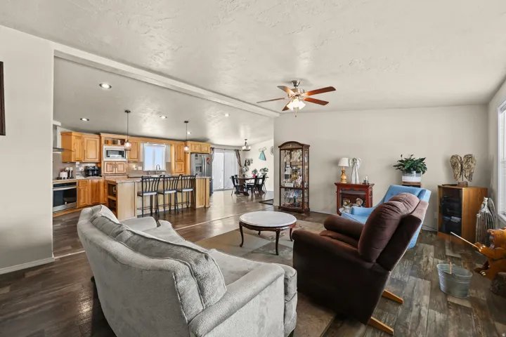 Open-concept design featuring wood-finish flooring, recessed lighting, a ceiling fan, and a kitchen with wood cabinetry and an island with seating