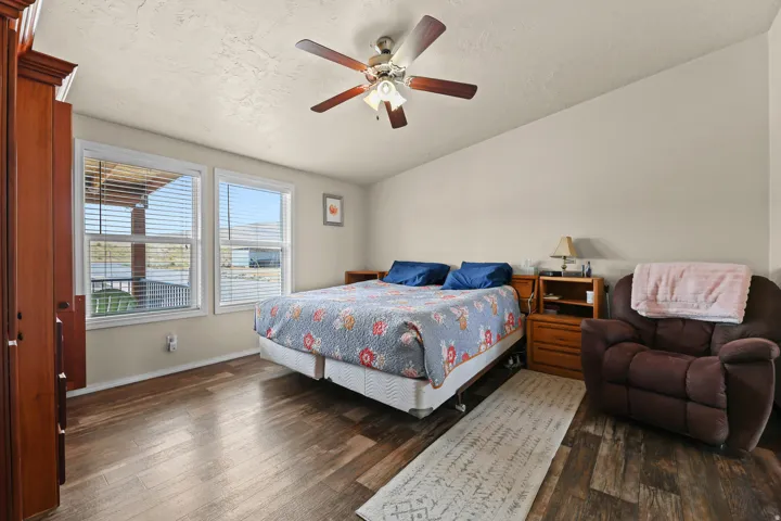 Wood-finish flooring, dual windows with horizontal blinds, sloped ceiling, and a ceiling fan