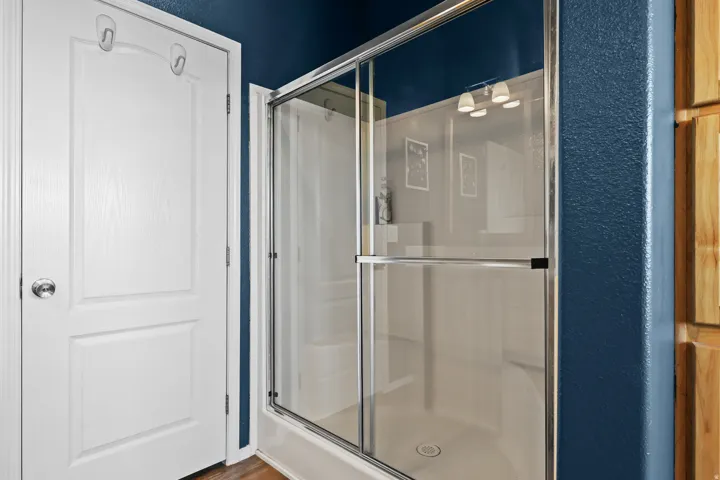 Frameless glass shower enclosure with chrome hardware, a built-in shower shelf, and a three-light vanity fixture