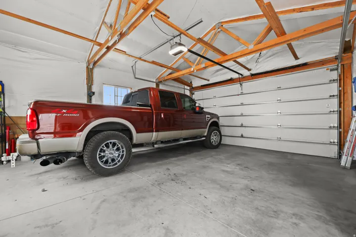 Spacious garage featuring concrete flooring, an automatic garage door opener, exposed ceiling trusses, and a side window