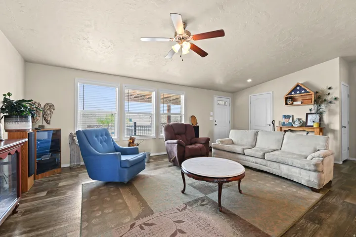 Spacious living area featuring wood-finish flooring, a ceiling fan, and multiple windows
