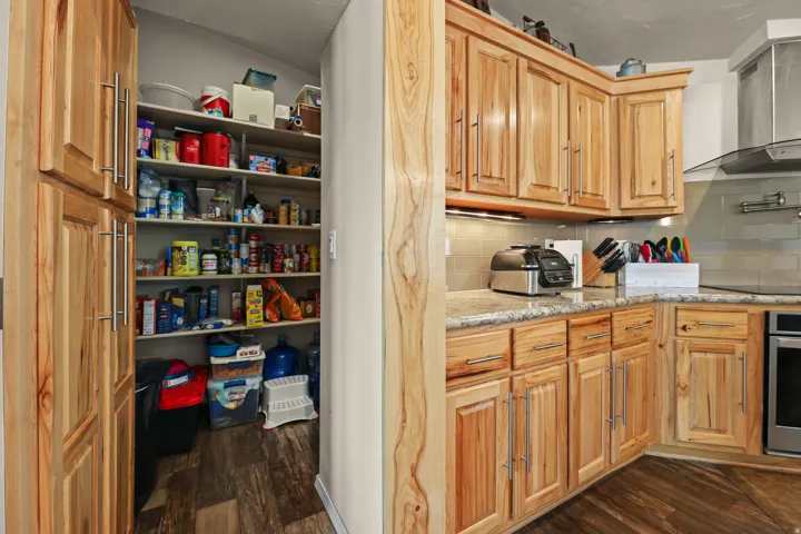 Wood-finish cabinetry with brushed nickel hardware, light-toned countertops, tile backsplash, and a stainless steel range hood