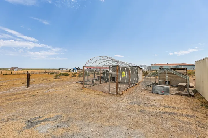 Expansive outdoor space featuring multiple animal enclosures, a galvanized metal trough, and a large storage building