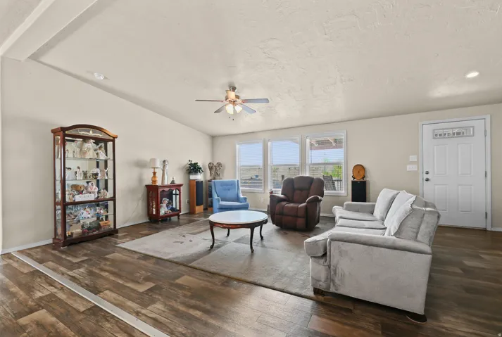 Spacious living area featuring wood-finish flooring, vaulted ceiling, ceiling fan, multiple windows, and a white paneled entry door with decorative glass