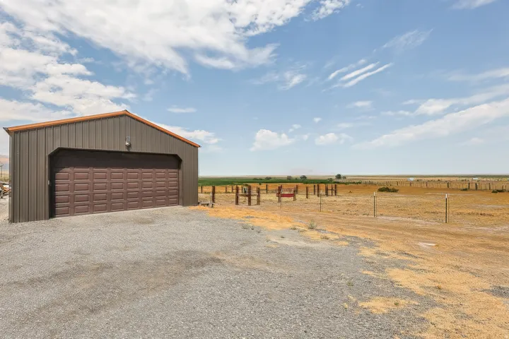 Metal-clad outbuilding with a brown garage door, gravel foreground, and expansive open terrain