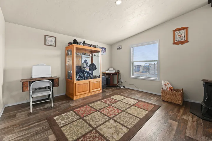 Vaulted ceiling with a recessed light fixture, neutral wall paint, wood-finish flooring, and a large window with blinds