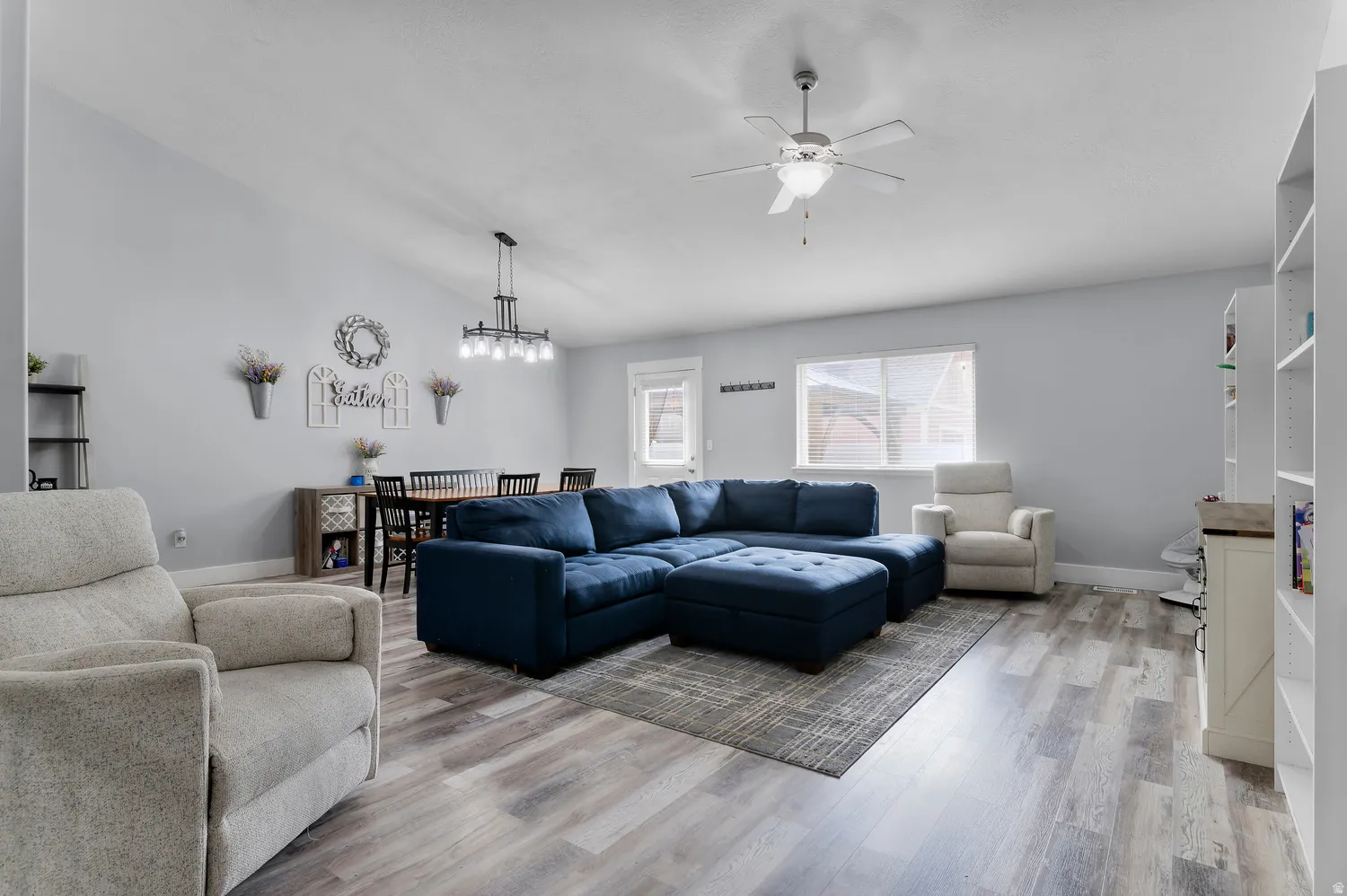 Vaulted ceiling, wood-finish flooring, ceiling fan, contemporary dining chandelier, and built-in shelving