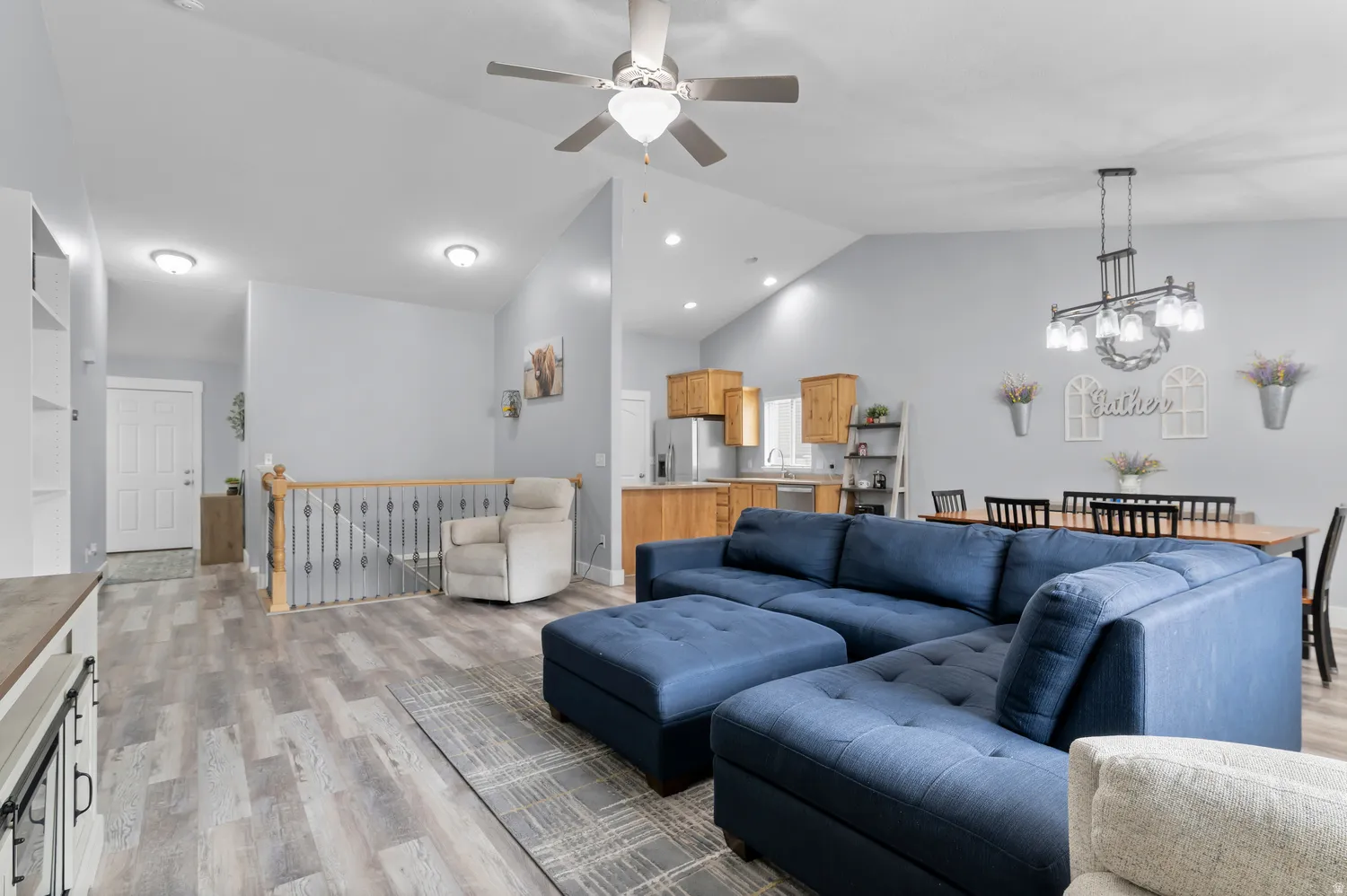Open-concept living space featuring vaulted ceilings, wood-finish flooring, a built-in shelving unit, and a ceiling fan with light