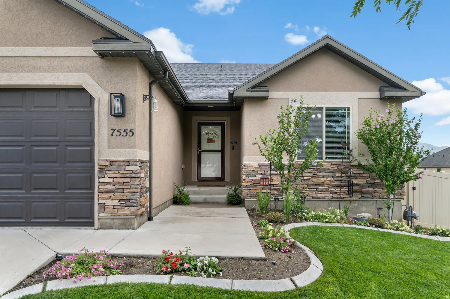Stucco exterior with stone veneer accents, an attached garage, landscaped front yard, and covered entry